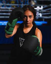 variant:Black/Green::TITLE Boxing Conquest Training Boxing Gloves on boxer's hands in fighting stance outside of boxing ring