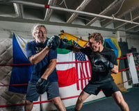 variant:lifestyle::TITLE Black Punch Mitts 2.0 boxer hitting mitts with trainer