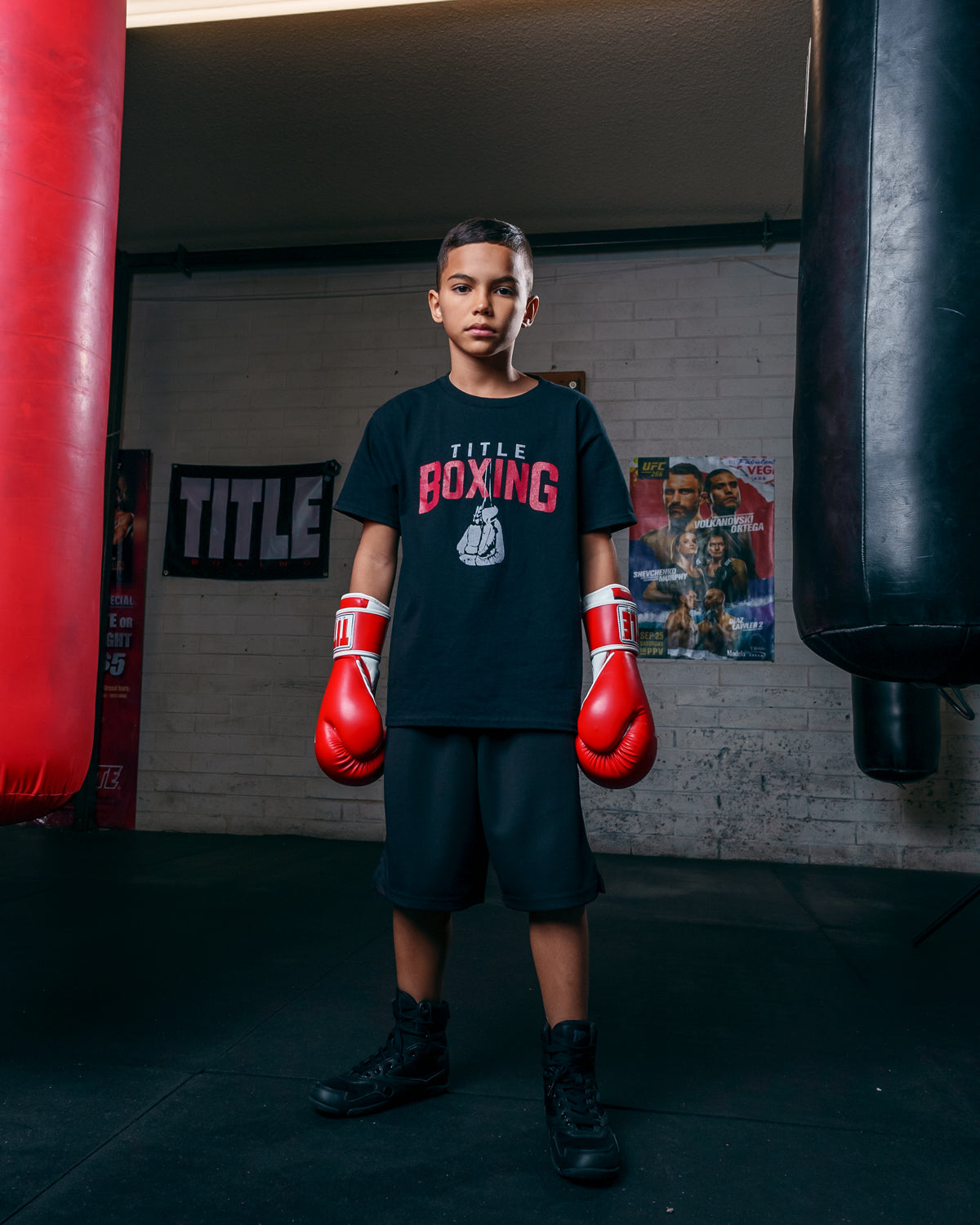 variant:red/white::TITLE Classic Pro Style Training Gloves 3.0 kid standing between 2 bags