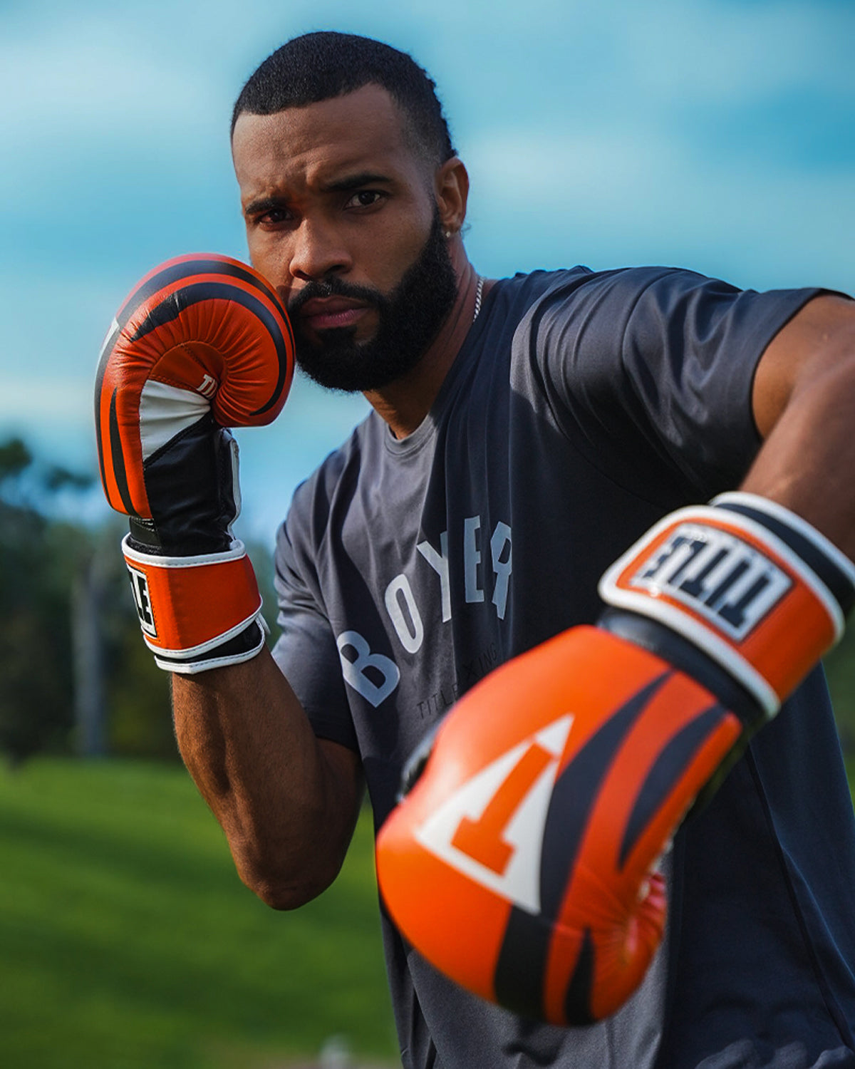variant:Orange/Black/White::TITLE Boxing World Bag Boxing Gloves on boxer's hands in fighting stance closeup