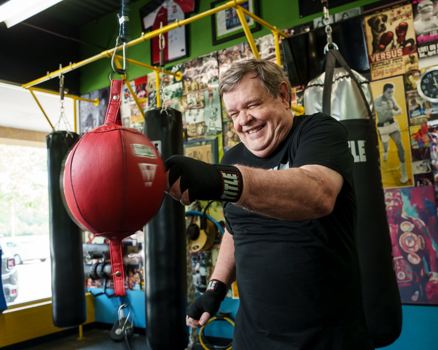 variant:black::TITLE Boxing Fight Back Semi-Elastic Hand Wraps guy hitting double end bag