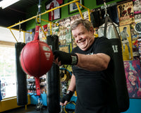 variant:black::TITLE Boxing Fight Back Semi-Elastic Hand Wraps guy hitting double end bag
