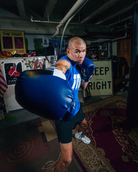 variant:Blue/Black::Fighting Sports Gloves and Wraps Bundle blue/black gloves on fighter in the gym second view