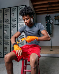 variant:lifestyle::Fighting Sports Gloves and Wraps Bundle fighter wrapping hands with orange wraps in locker room