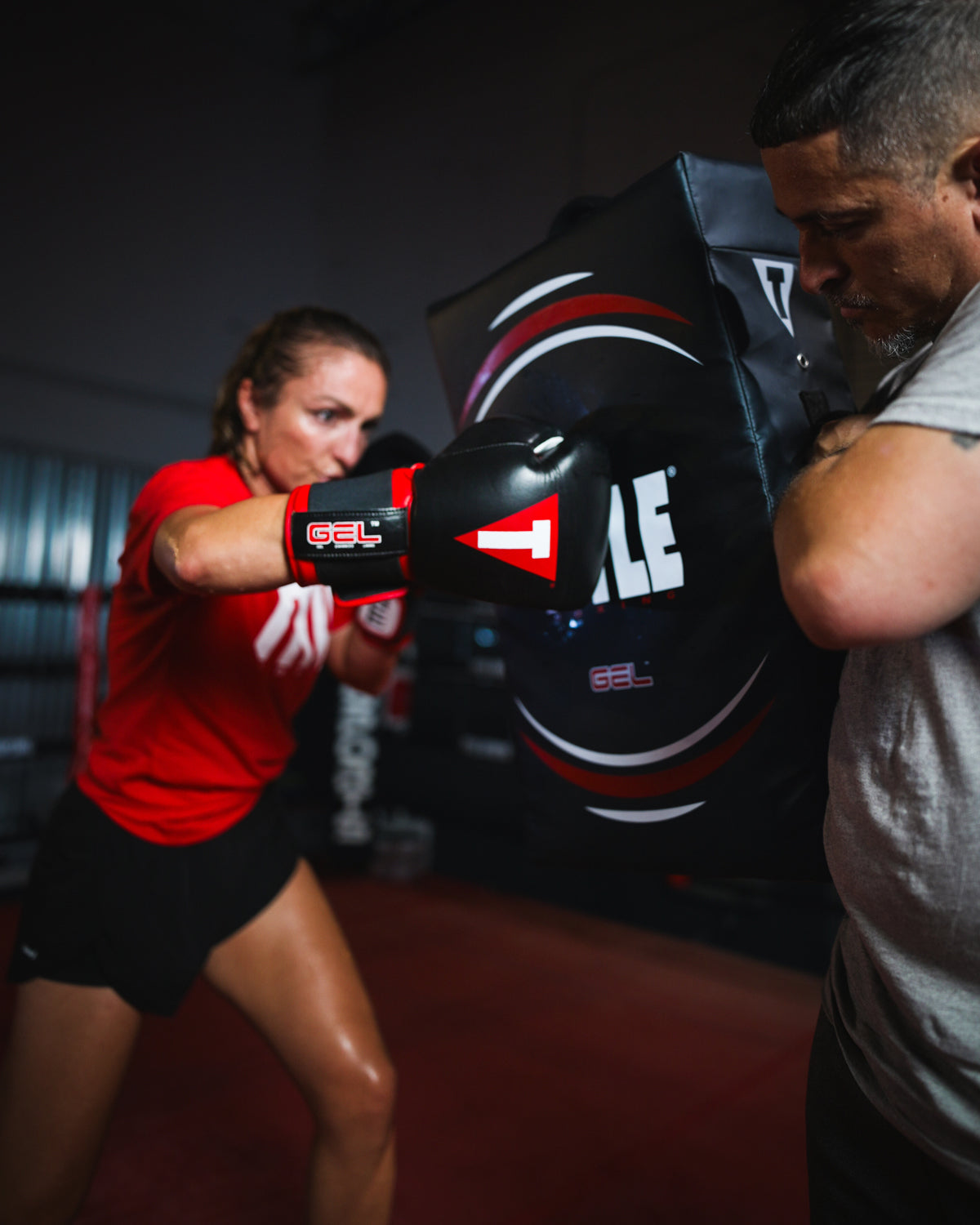 variant:lifestyle::TITLE Boxing Gel Ripple Strike Shield being held by boxing coach with boxer punching shield