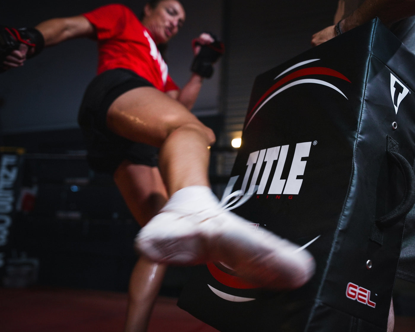 variant:lifestyle::TITLE Boxing Gel Ripple Strike Shield being held by boxing coach with boxer kicking shield