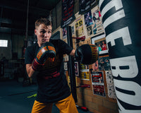 variant:black/red::KRONK Boxing Leather Bag Gloves kid hitting bag looking at camera