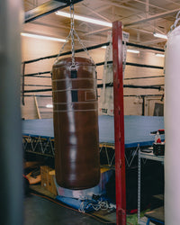 variant:brown::TITLE Boxing KO-Vert Leather Heavy Bag hanging in the gym in front of a boxing ring