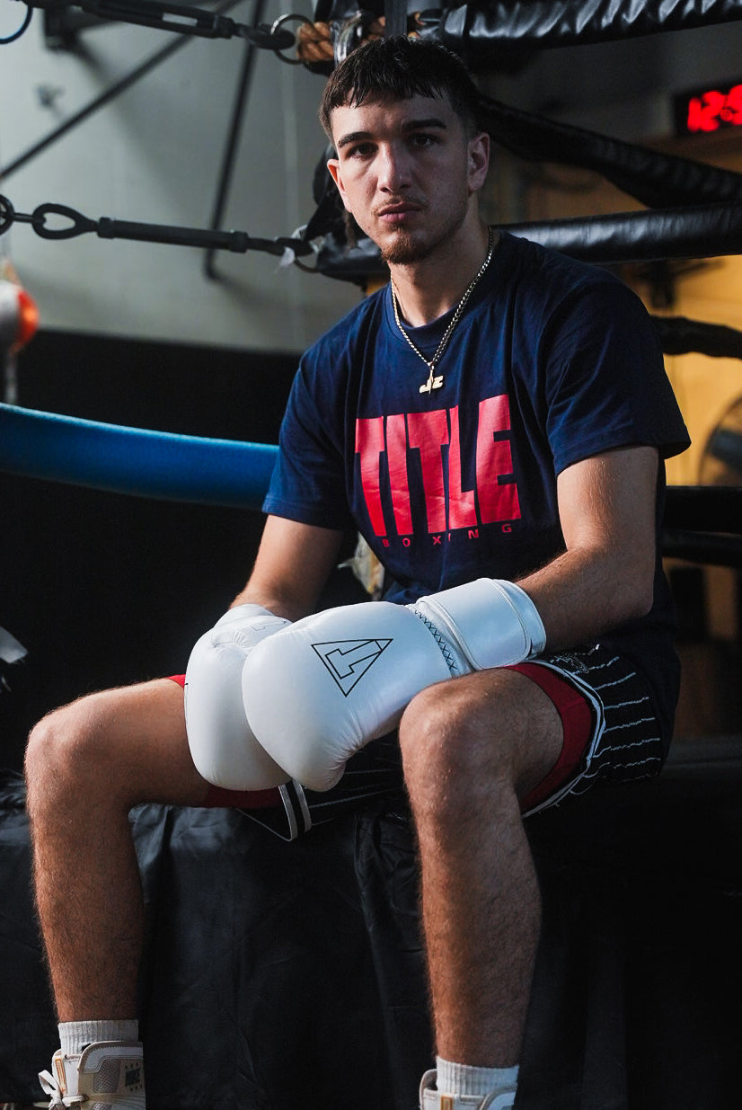 variant:white::TITLE Boxing Momentum Pro Bag Gloves on boxer's hands in front of ring