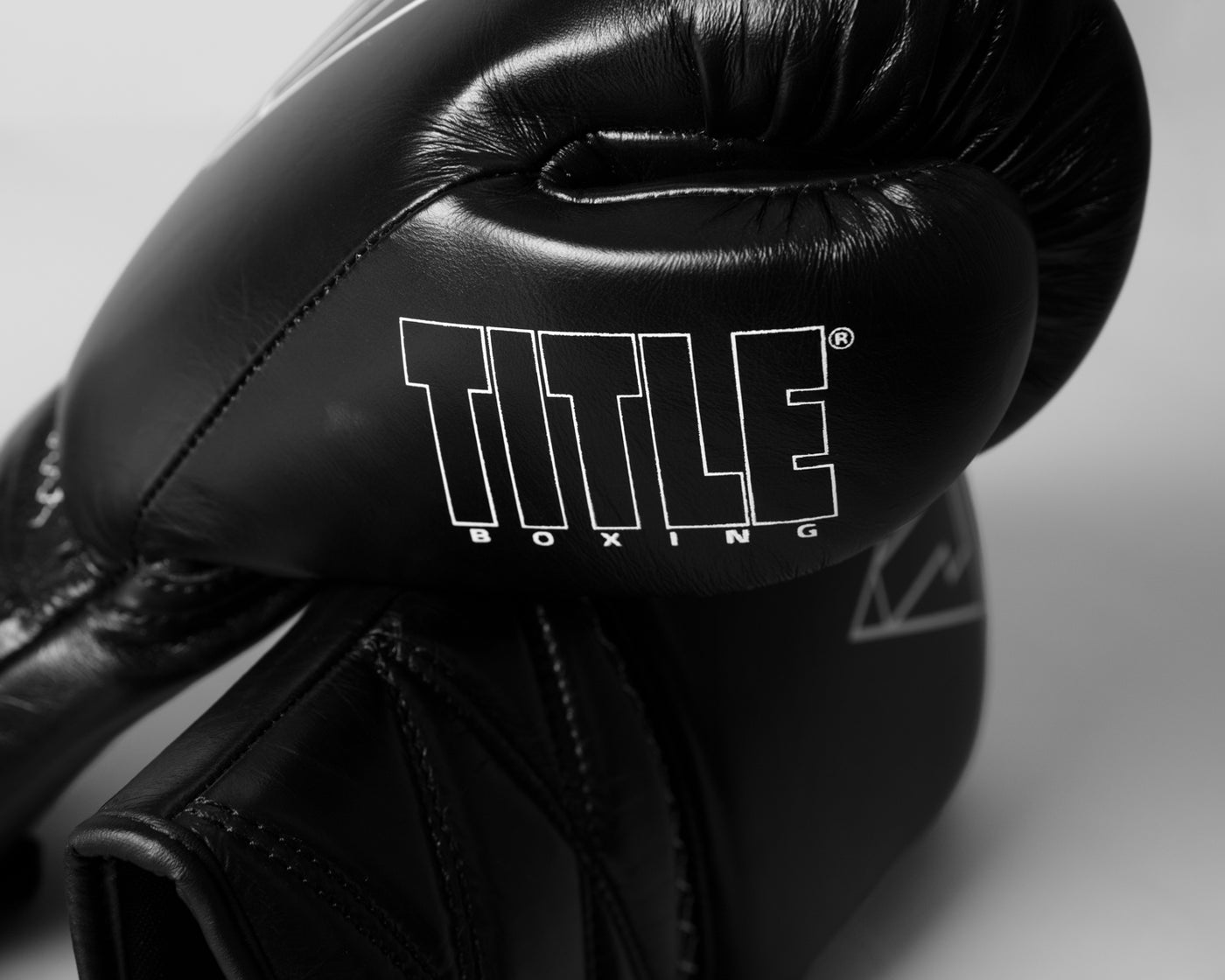 variant:black::TITLE Boxing Momentum Pro Sparring Gloves closeup of TITLE Boxing logo on thumb