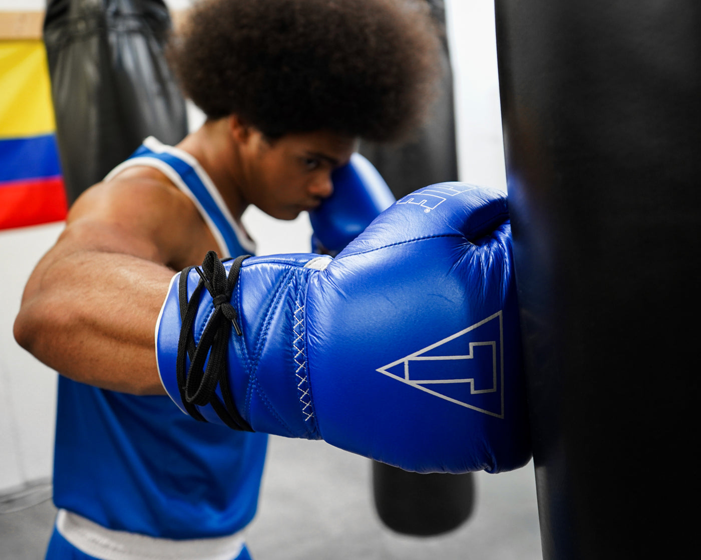 variant:blue/silver::TITLE Boxing Momentum Pro Sparring Gloves on boxer's hands hitting bag at the gym