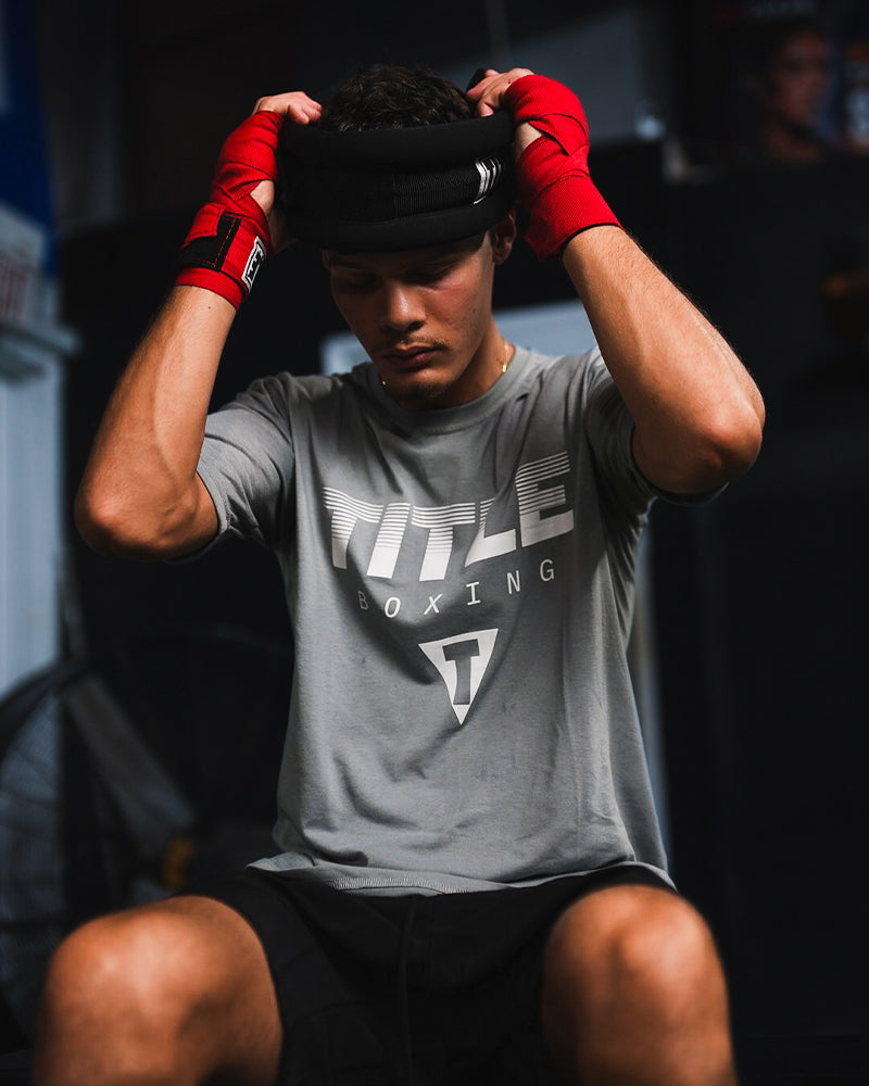 variant:lifestyle::TITLE Boxing Neck Strengthener 2.0 being placed on man's head in the gym