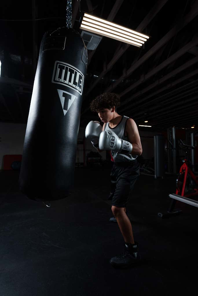 variant:lifestyle::TITLE Boxing Professional Choice 125lb Synthetic Leather Heavy Bag guy hitting bag silver promex gloves
