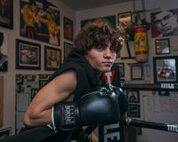 variant:black::TITLE Boxing Old School Leather Bag Gloves 2.0 kid leaning on ring