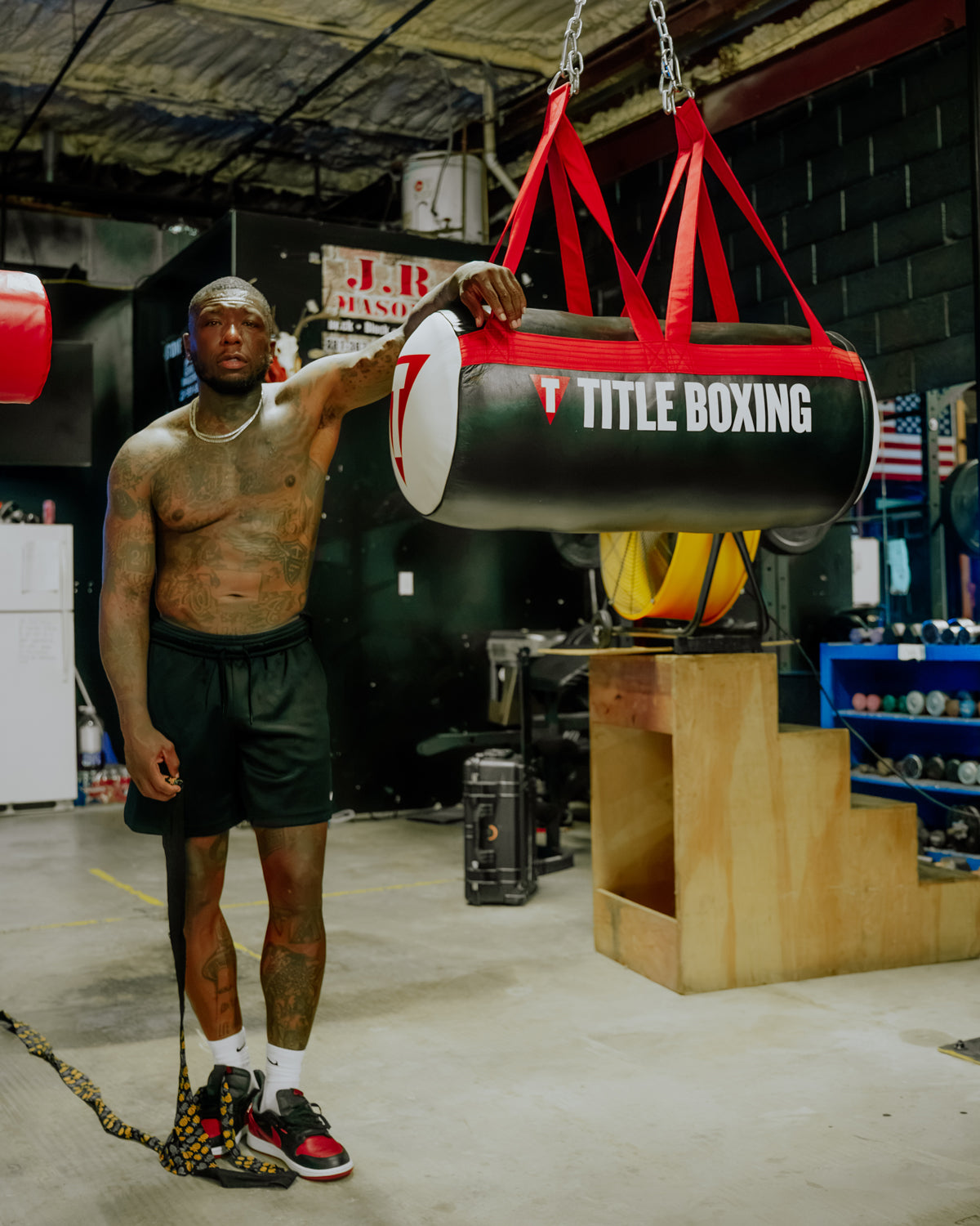variant:lifestyle::TITLE Boxing Premier Leather Uppercut Bag hanging in the gym with boxer standing next to it