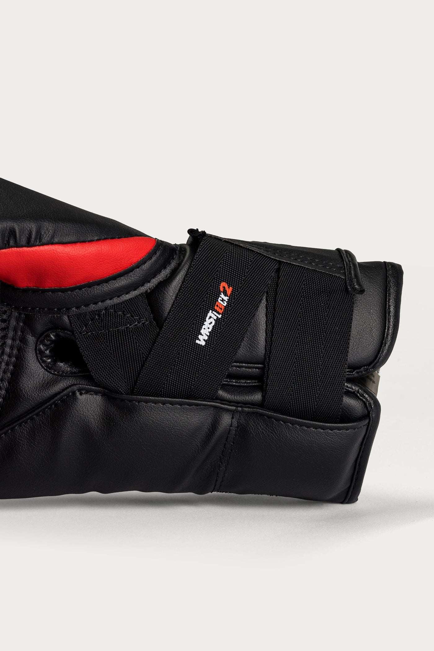variant:red::Close-up of a black leather martial arts glove with a red interior lining and a black elastic strap featuring the 'WRESTLE Z' logo, set against a light gray background.