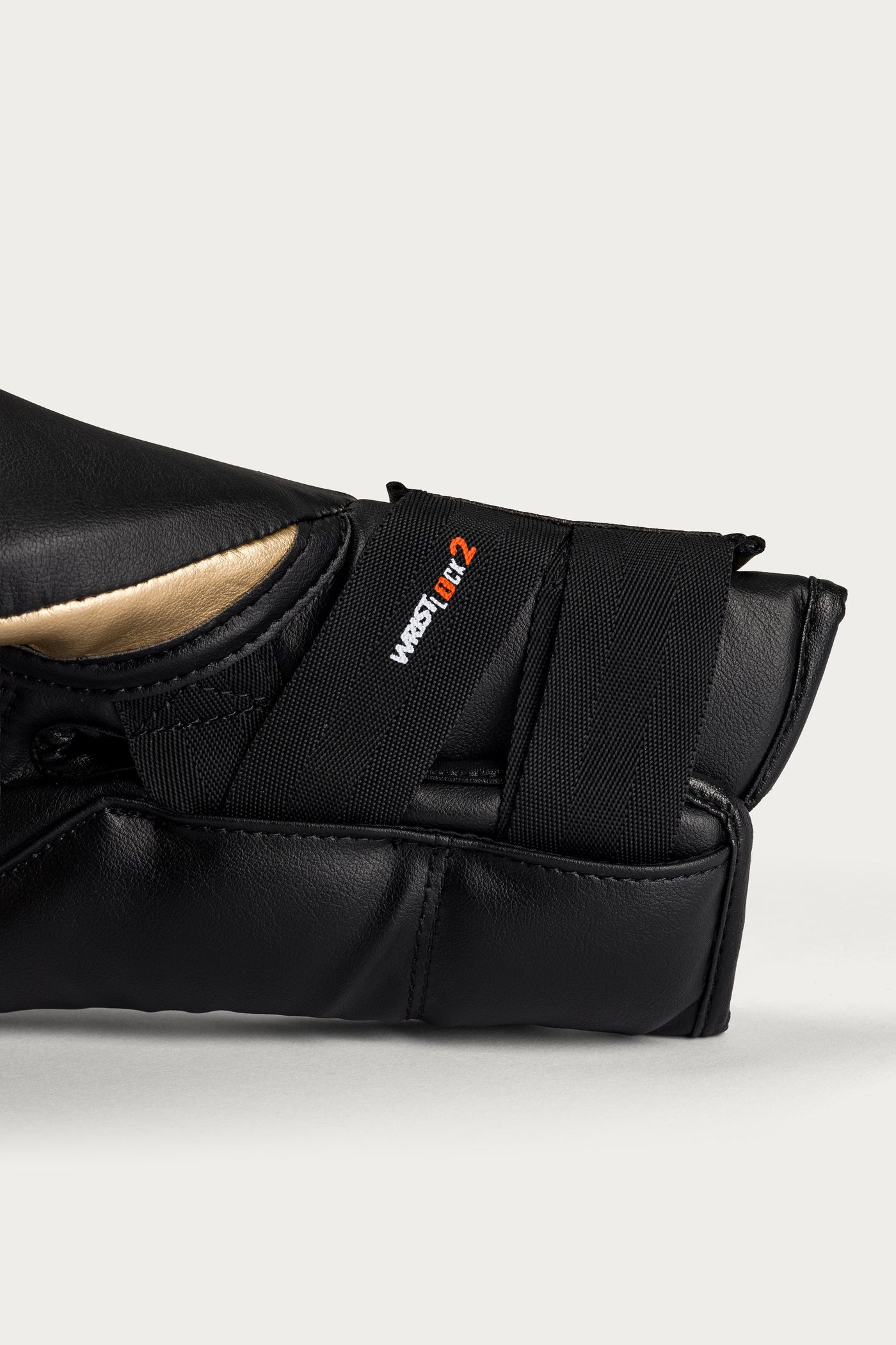 variant:Gold::Close-up of a black martial arts grappling sleeve with a hook-and-loop strap closure, featuring the West 1st 2 logo in white and orange, set against a light gray background.