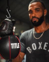 variant:lifestyle::TITLE Boxing Rubber Double End Bag Cable closeup of cable with boxer holding double end bag in the gym