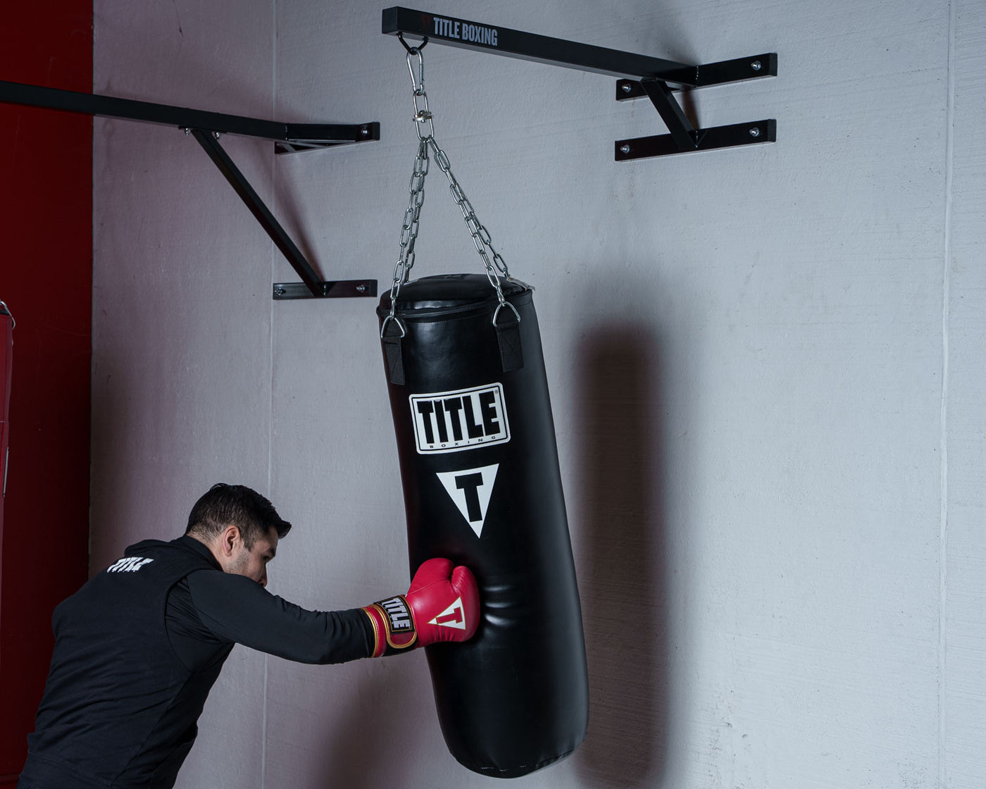 variant:lifestyle::TITLE Boxing Space Saver Wall Mount Bag Hanger 2.0 with a boxer using a heavy bag