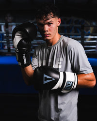 variant:Black/White::TITLE Boxing Swift Bag Boxing Gloves on boxer's hands in fighting stance in front of a ring