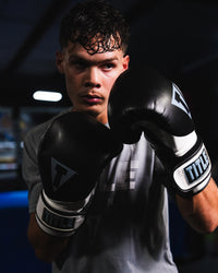 variant:Black/White::TITLE Boxing Swift Bag Boxing Gloves closeup on boxer's hands in fighting stance in front of a ring