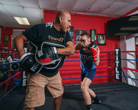 variant:lifestyle::TITLE Boxing Aerovent Excel Incredi-Mitts 2.0 boxer and coach hitting back and forth girl and coach 