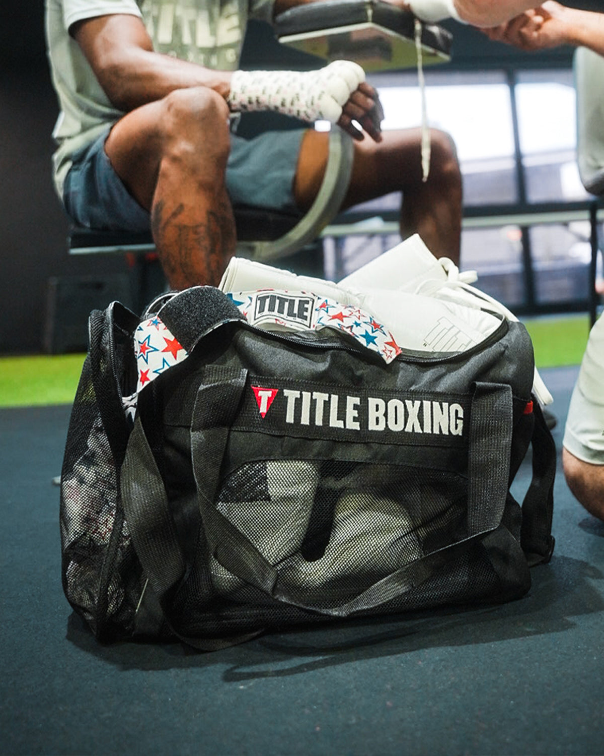 variant:lifestyle::TITLE Boxing Ventilated Sport Bag on floor of ring with fighter in background getting hands wrapped