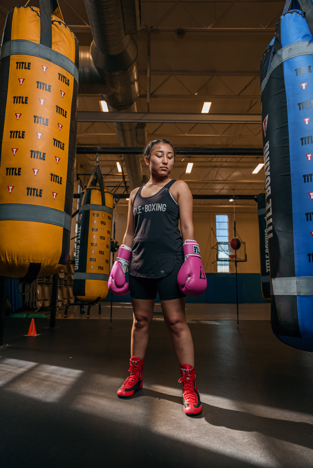 variant:Red/Black::TITLE Boxing Speed-Flex Encore Mid-Top Shoes girl with pink gloves on between 2 bags