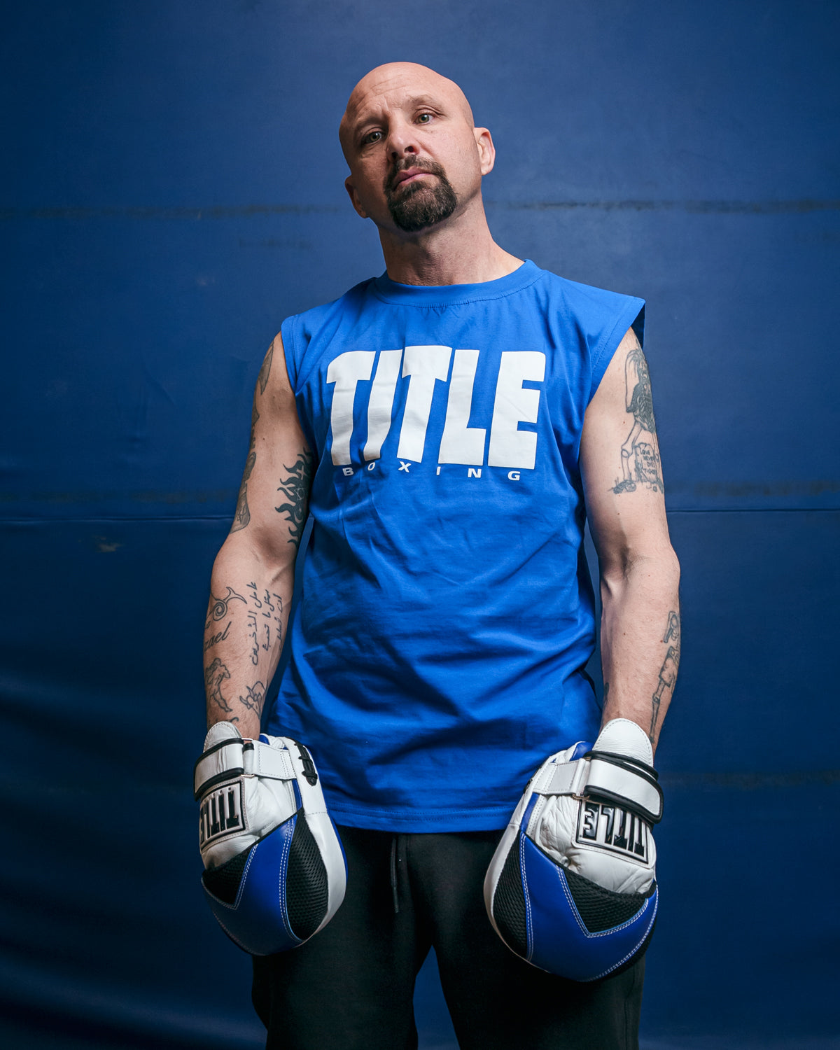 variant:Blue/White::TITLE Boxing Iconic Block Muscle Tee man posing in tee and punch mitts blue background