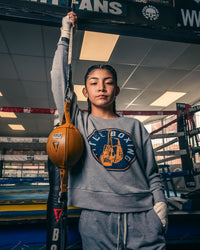 variant:Grey::TITLE Boxing Women's Signal Crewneck Sweatshirt girl in a pose holding double end bag cord