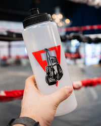 variant:lifestyle::TITLE Boxing Pro Plus Water Bottle being held in front of a boxing ring