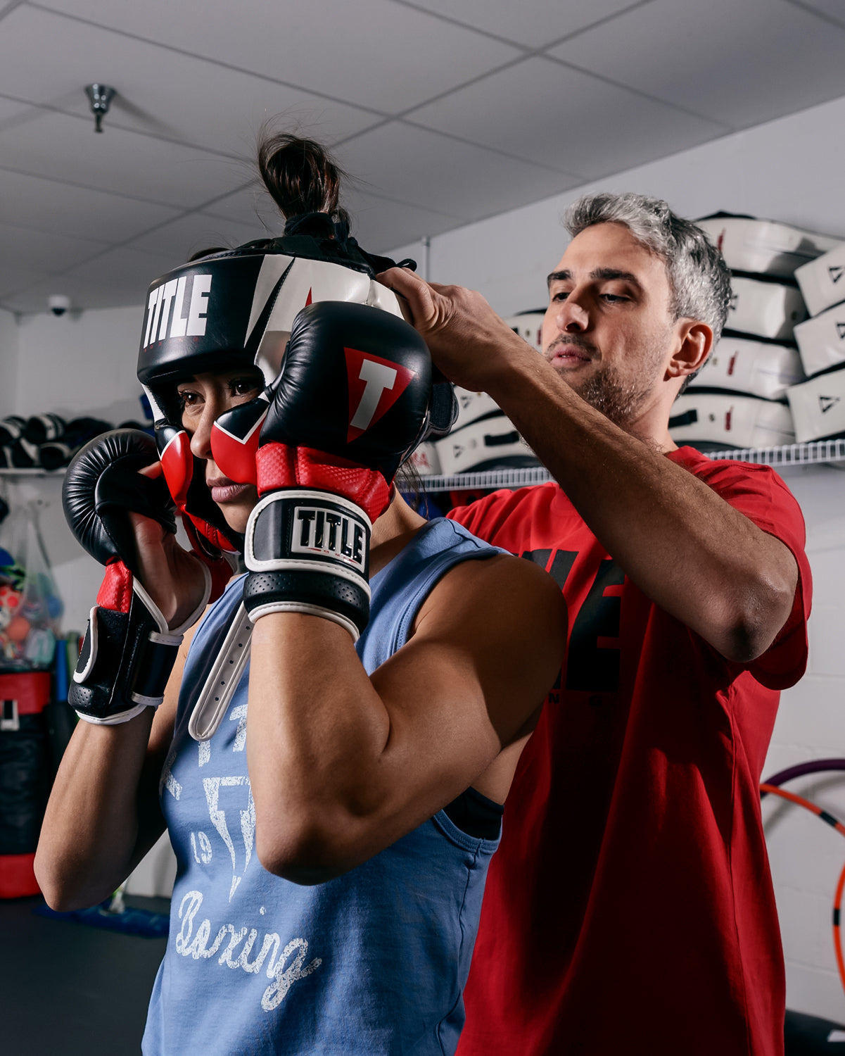 variant:lifestyle::TITLE MMA Command Training Headgear coach putting on headgear on girl