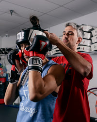 variant:lifestyle::TITLE MMA Command Training Headgear coach putting on headgear on girl