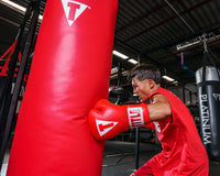 variant:red::TITLE Classic Super Bag Gloves 2.0 kid hitting red bag with red gloves 