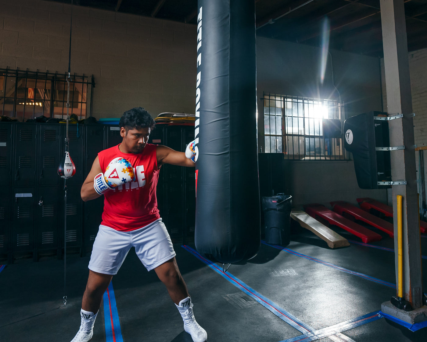 variant:lifestyle::TITLE Boxing Gel World V2T Limited Edition Autism Awareness Bag Gloves guy wearing boxing gloves in boxing gym with heavy bag