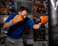 variant:orange::TITLE Boxing Gel World V2T Bag Gloves guy wearing boxing gloves hitting heavy bag