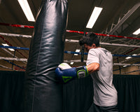 variant:navy/grey::TITLE Boxing Gel World V2T Bag Gloves kid wearing boxing gloves hitting heavy bag