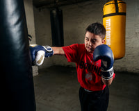 variant:navy/white::TITLE Boxing Gel World V2T Bag Gloves kid wearing boxing gloves hitting heavy bag
