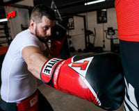variant:red/black::TITLE Boxing Infused Foam Interrogate Training Gloves 2.0 guy wearing boxing gloves punching heavy bag