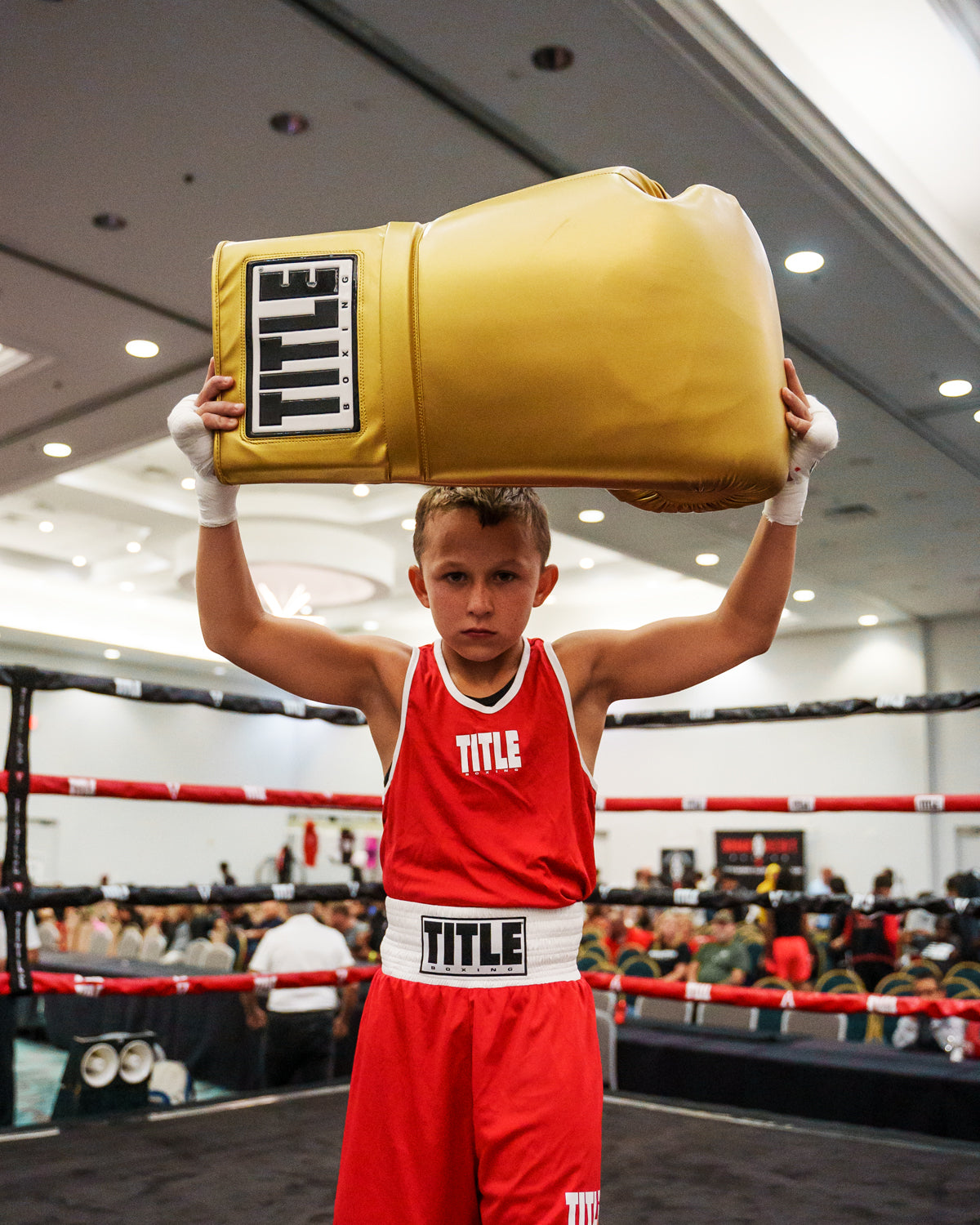 variant:gold::TITLE Boxing Jumbo Boxing Gloves 2.0 kid posing with jumbo boxing gloves in boxing ring
