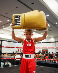 variant:gold::TITLE Boxing Jumbo Boxing Gloves 2.0 kid posing with jumbo boxing gloves in boxing ring