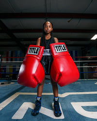 variant:red::TITLE Boxing Jumbo Boxing Gloves 2.0 kid posing with jumbo boxing gloves in boxing ring
