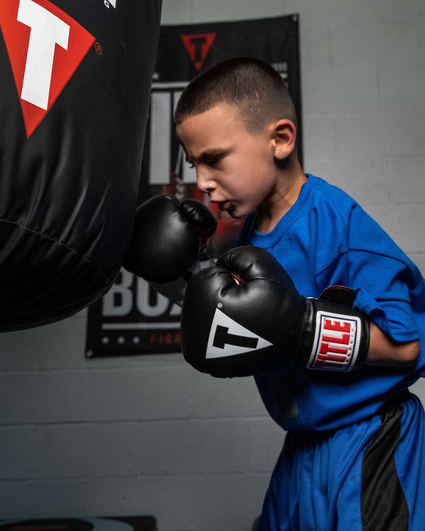 variant:black/white/red::TITLE Classic Kid & Youth Boxing Gloves 2.0 kid wearing boxing gloves with heavy bag