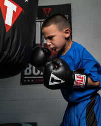 variant:black/white/red::TITLE Classic Kid & Youth Boxing Gloves 2.0 kid wearing boxing gloves with heavy bag