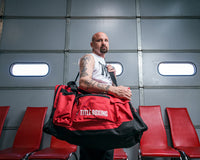 variant:red::TITLE Boxing Deluxe Gear Bag guy carrying bag infront of door