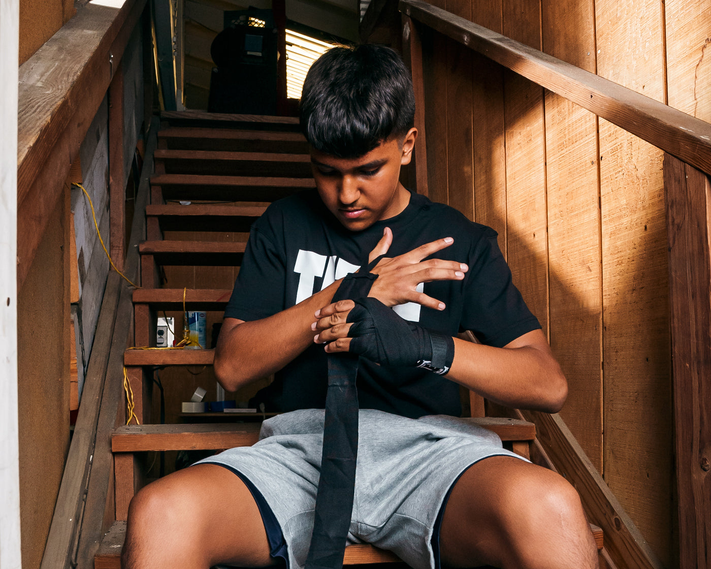 variant:lifestyle::TITLE Boxing Advanced Semi-Elastic Assorted Hand Wraps (10 Pair) boxer wrapping hands in black hand wrap
