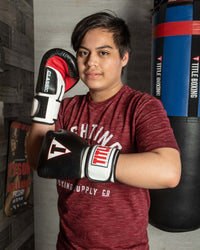 variant:black/white/red::TITLE Classic Leather Super Bag Gloves 2.0 kid standing infront of blue bag