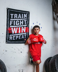 variant:lifestyle::TITLE Boxing Train Fight Win Repeat Banner behind a youth boxer