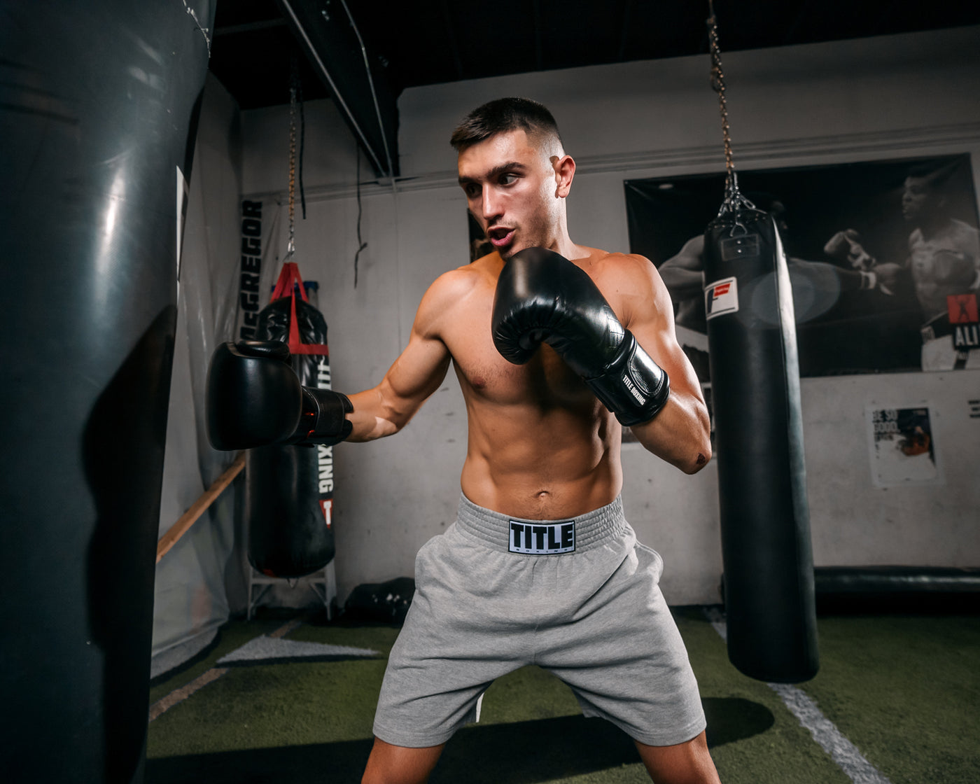 variant:black::TITLE Boxing Ko-Vert Bag Gloves guy boxing wearing boxing gloves in gym with heavy bags