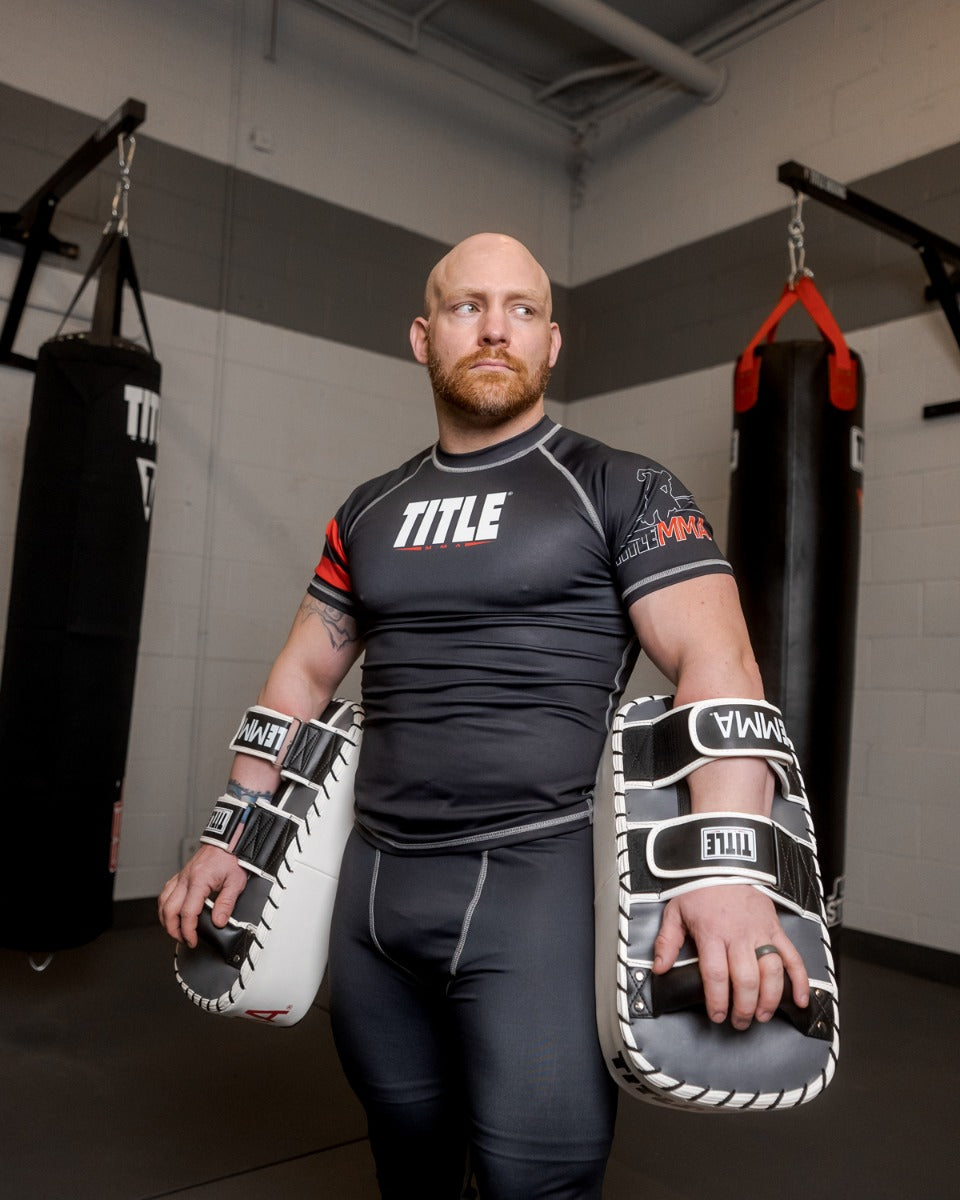 variant:black/white/grey::TITLE MMA Air Raid Thai Pads (Pair) guy holding pads down